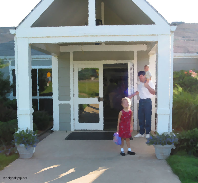 a child stands in front of a man with another child on his shoulders standing in front of a school entrance